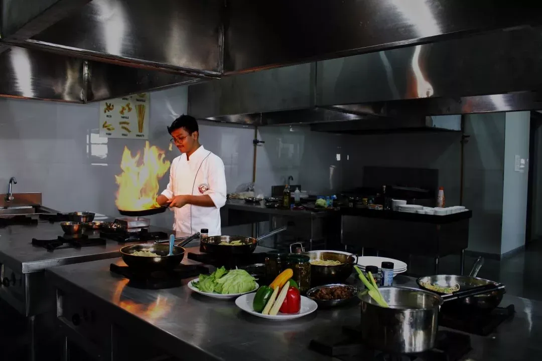 A hospitality student flambéing a pan in the campus training kitchen